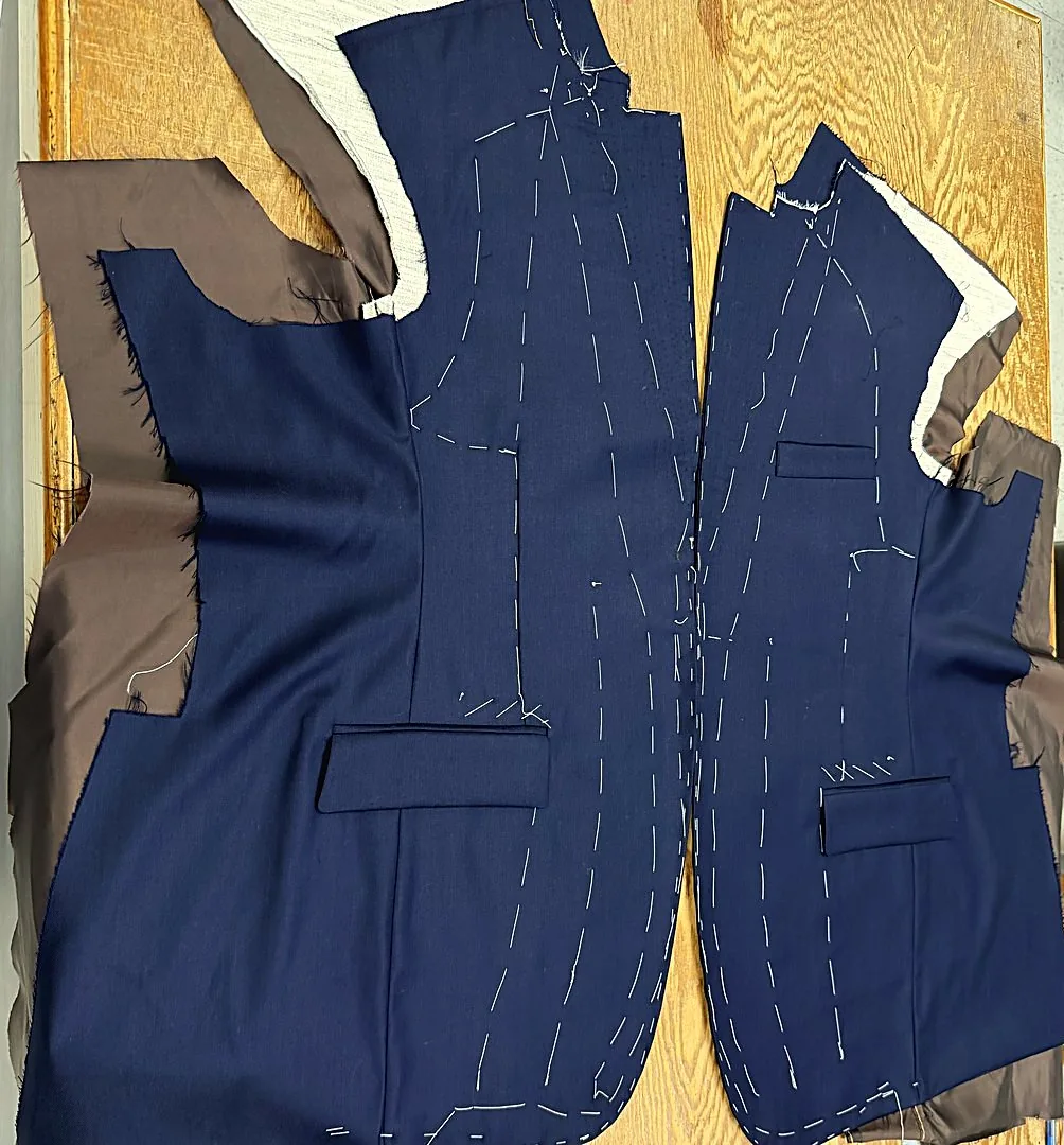 Navy jacket fronts with hand basting and pale canvas at the edges, on the bench